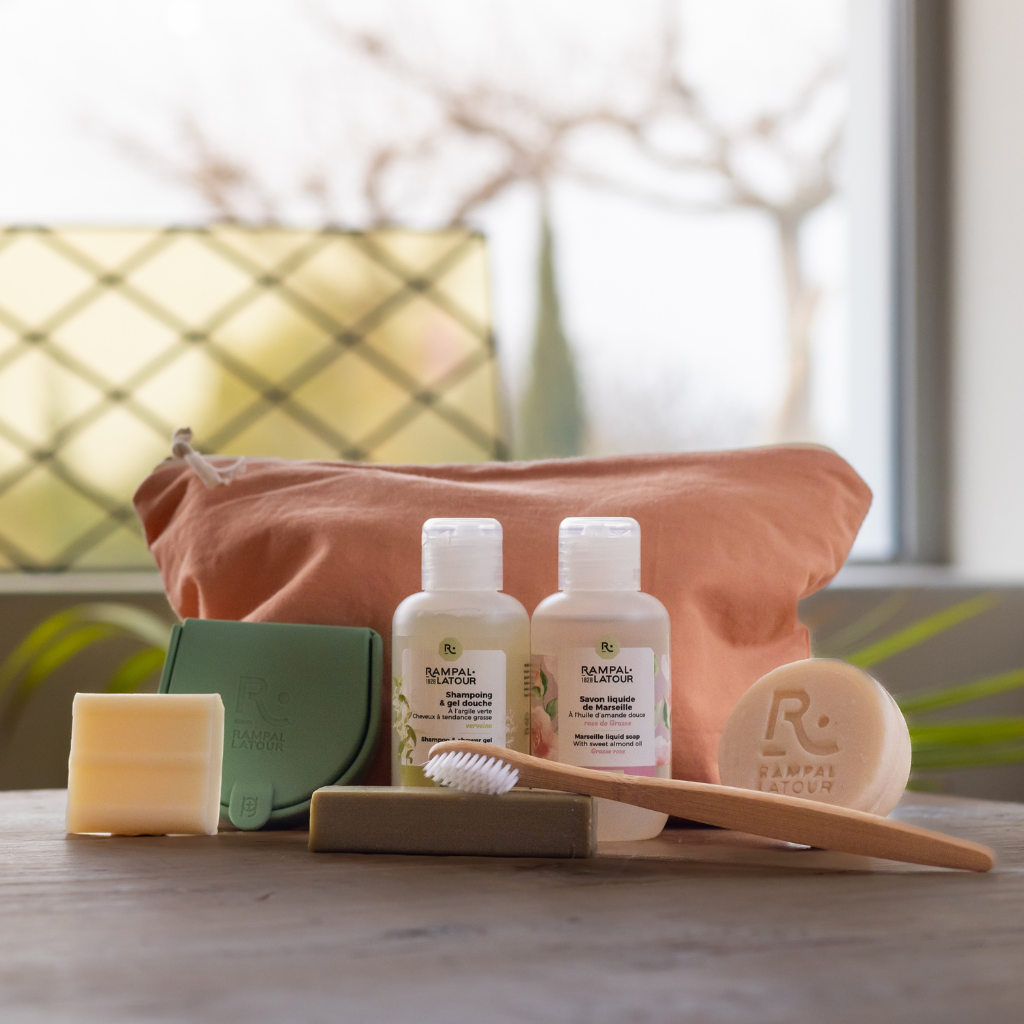 Trousse de voyage avec savons de Marseille, shampoing et savon liquide Rampal Latour posés sur une table